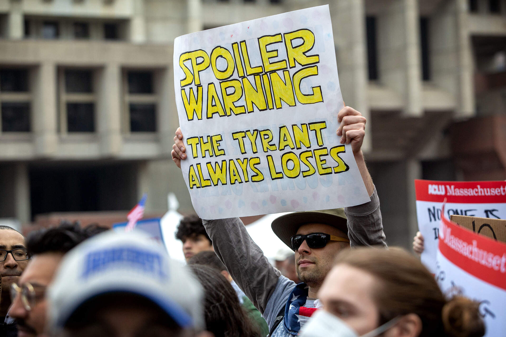 A protester at the Service Employees International Union solidarity rally at Boston City Hall Plaza holds up a protest placard. (Robin Lubbock/WBUR)