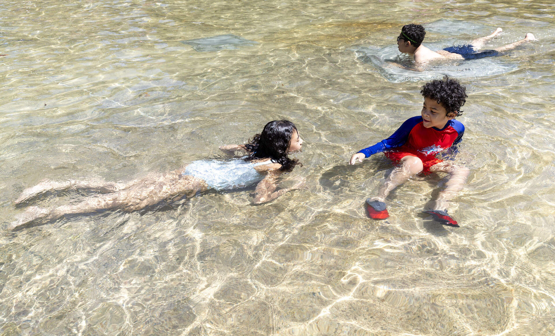 Isabella Rodriguez chases her brother Noah through the cool water of the Frog Pond, on the pond's opening day on Boston Common. (Robin Lubbock/WBUR)