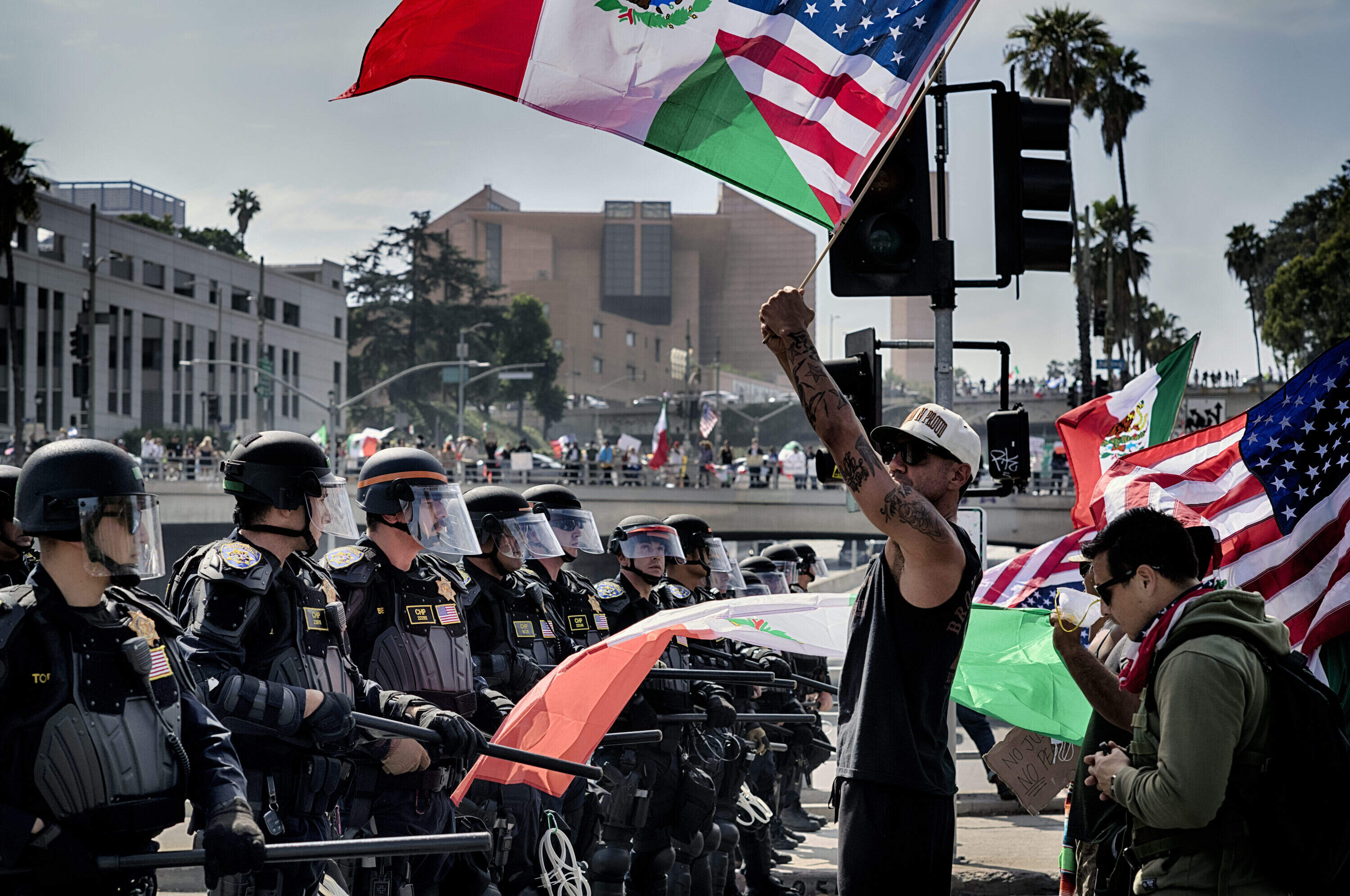 Protesters wave flags against California Highway Patrol officers with ready batons blocking a freeway overpass during a "No Kings" protest in downtown Los Angeles on Saturday, June 14, 2025. (Richard Vogel/AP)