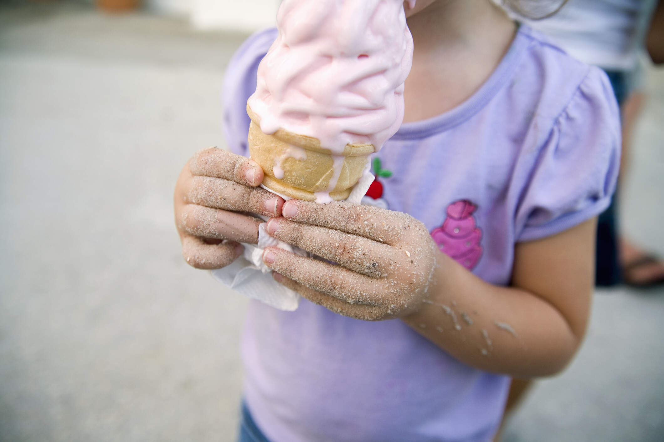 Young girl holding an ice cream cone, with sand sticking to her hands. (Getty Images)