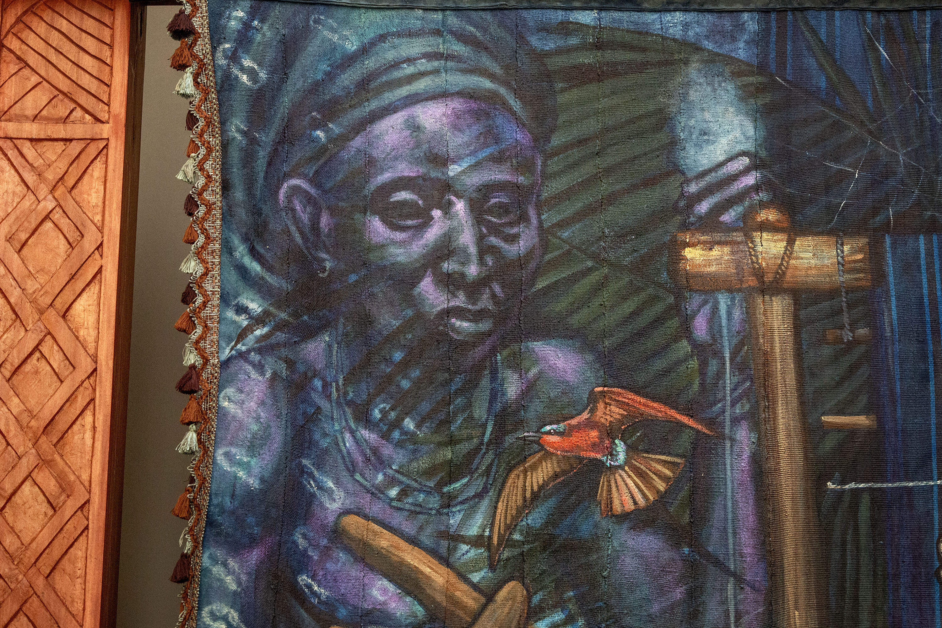 A deity watches over the weavers as a carmine bee-eater flies by, in Stephen Hamilton's "Under the Spider's Web" installation. (Robin Lubbock/WBUR)