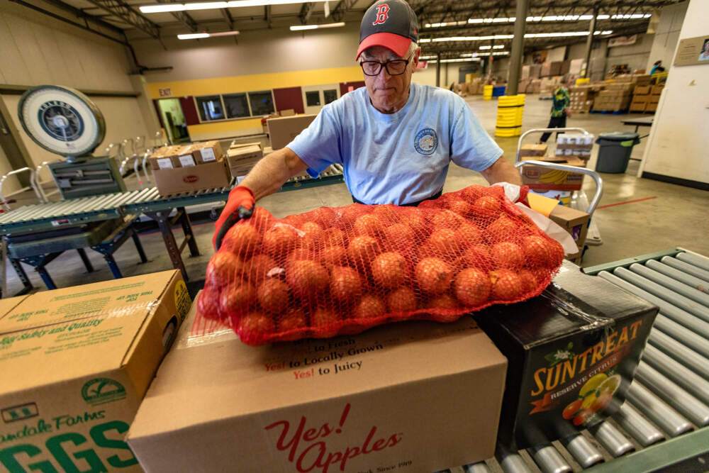 Northborough Food Pantry volunteer Norm Corbin places a bag of onions onto a conveyor to add to the order of food he is picking up from the Worcester County Food Bank in Shrewsbury. (Jesse Costa/WBUR)