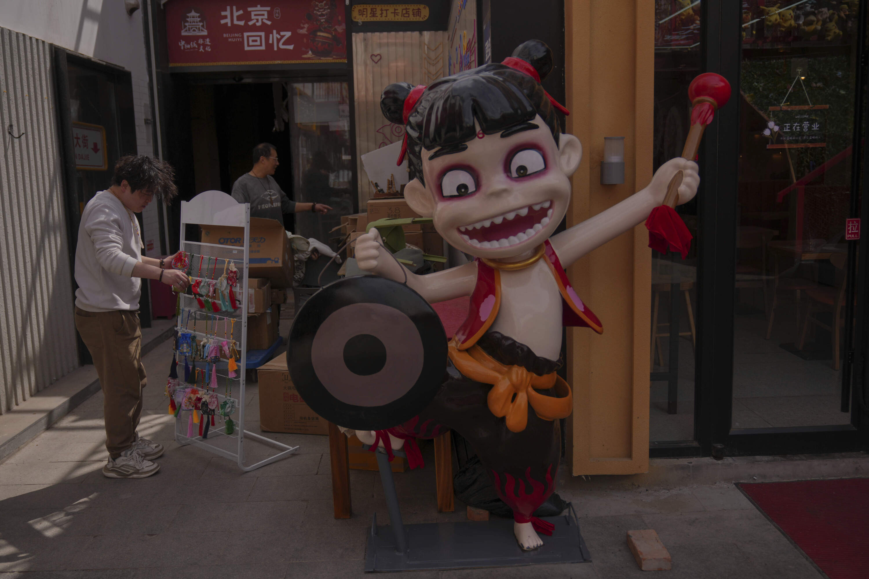 Workers places accessaries on a rack from boxes of stock near a cartoon character figure from the Chinese popular animated blockbuster movie "Ne Zha 2" in Beijing, Tuesday, April 1, 2025. (Andy Wong/AP)