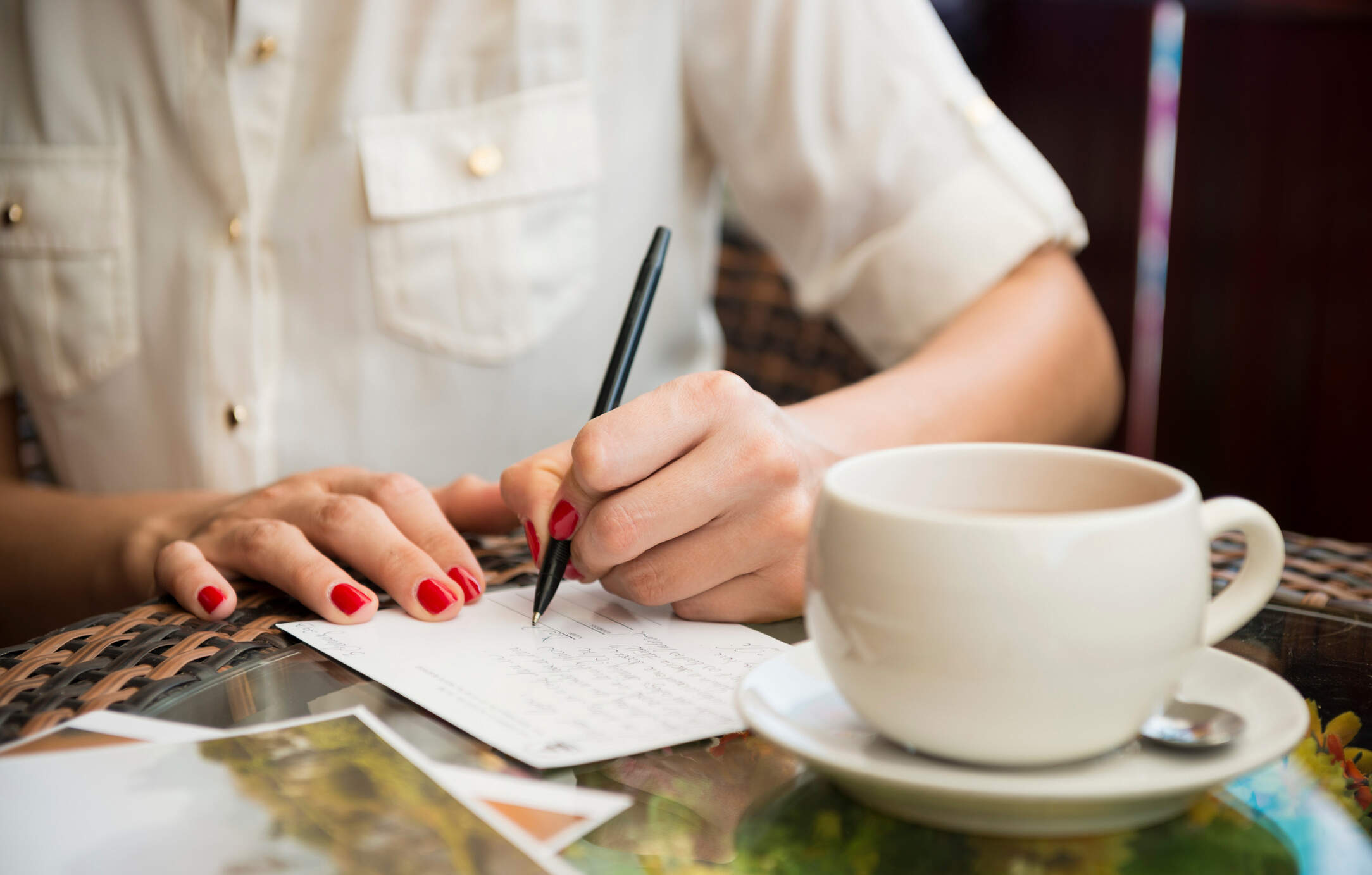 A woman writes postcards while she drinks coffee. (Getty Images)