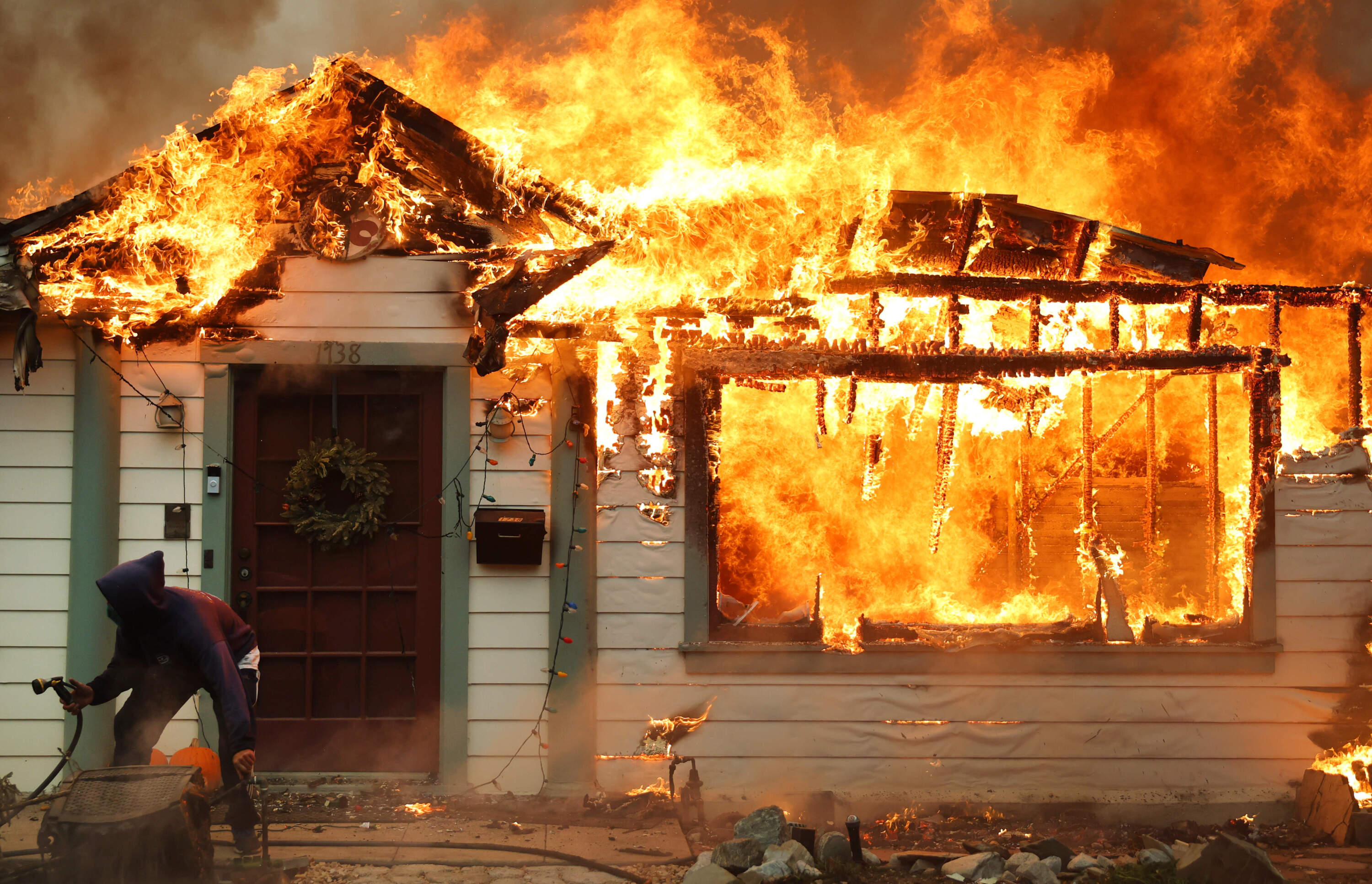 A person turns on a garden hose in an effort to save a neighboring home from catching fire during the Eaton Fire on Jan. 8, 2025 in Altadena, California. (Mario Tama/Getty Images)