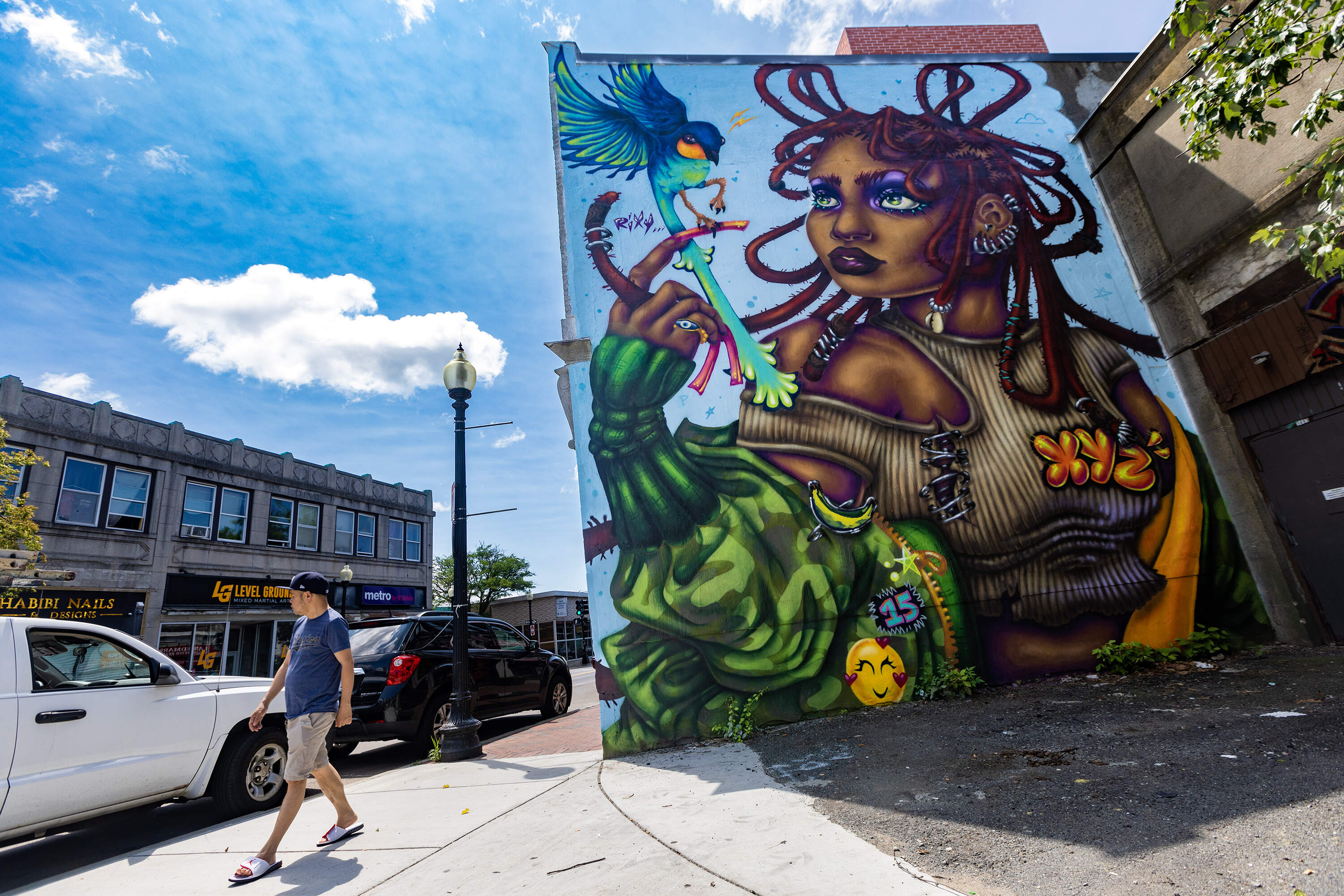 A man walks past “Reaching for the Stars,” a mural outside the MBTA Fields Corner station on Dorchester Avenue painted by the artist Rixy. (Jesse Costa/WBUR)
