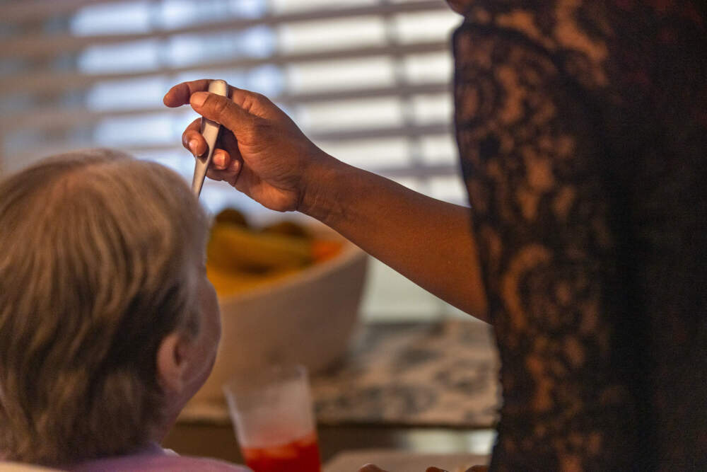 A Haitian worker feeds a resident at the Road to Responsibility group home in Marshfield. (Jesse Costa/WBUR)