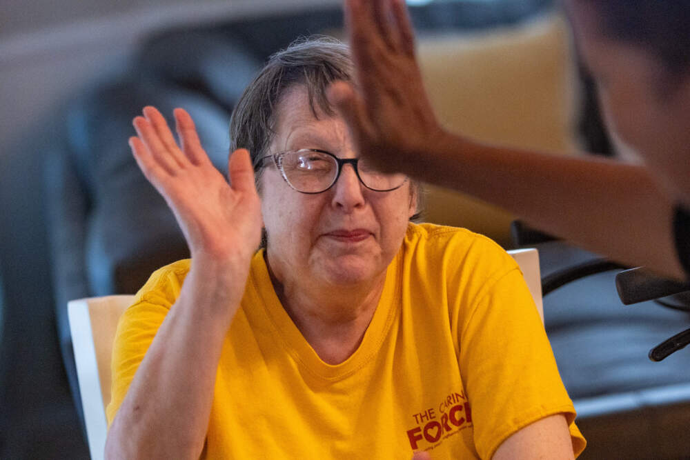 Resident Margie Hoffman gets a high five from a Haitian worker during dinner at the Road to Responsibility group home in Marshfield. (Jesse Costa/WBUR)