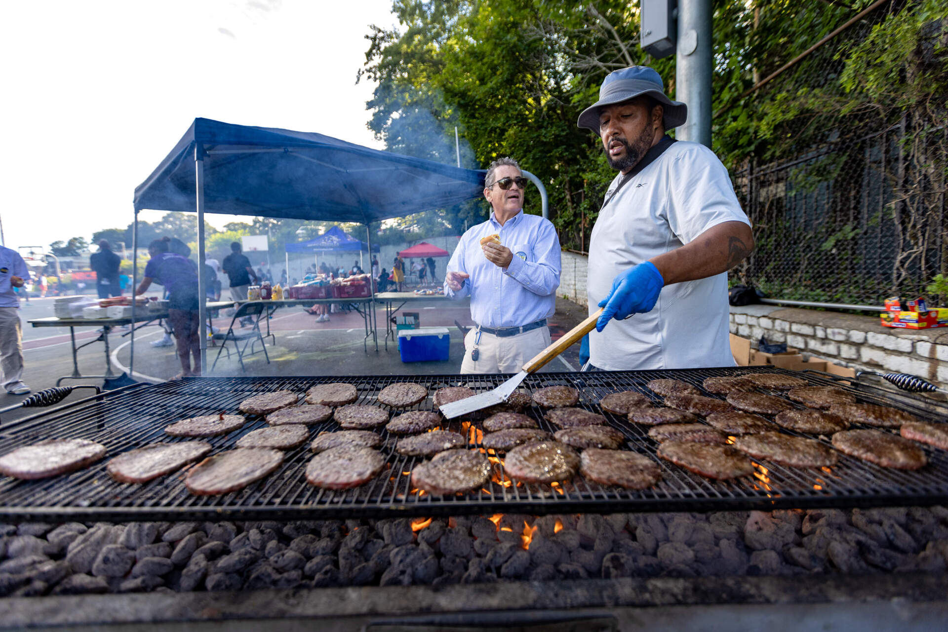 Mayoral candidate Domingos DaRosa chats with Boston City Council at-large candidate Frank Baker while he flips burgers at a community cookout at Ronan Park in Dorchester. (Jesse Costa/WBUR)