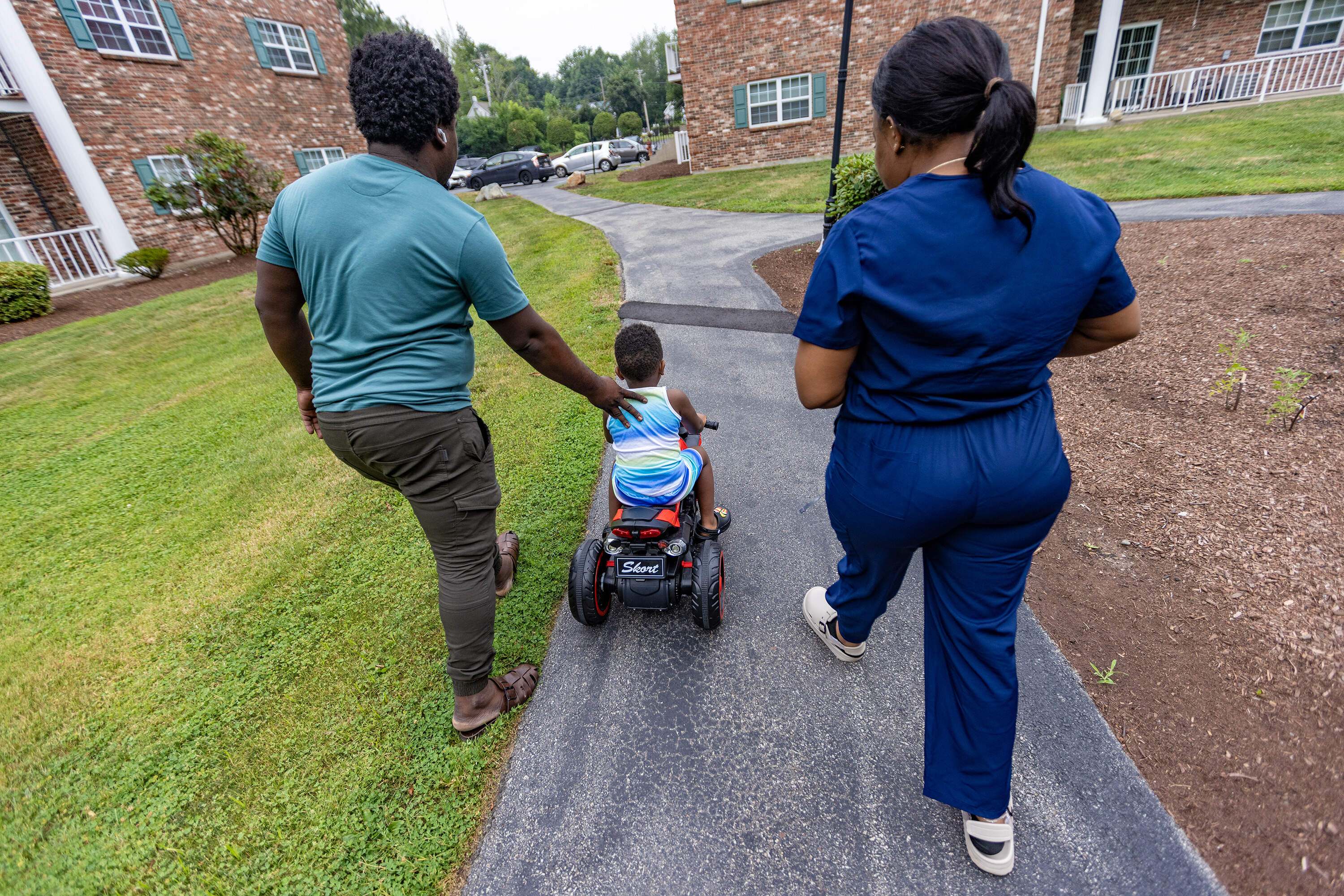 Jacques and Ivanne walk with their 3-year-old son while he rides his motorized trike near their home in Randolph. (Jesse Costa/WBUR)