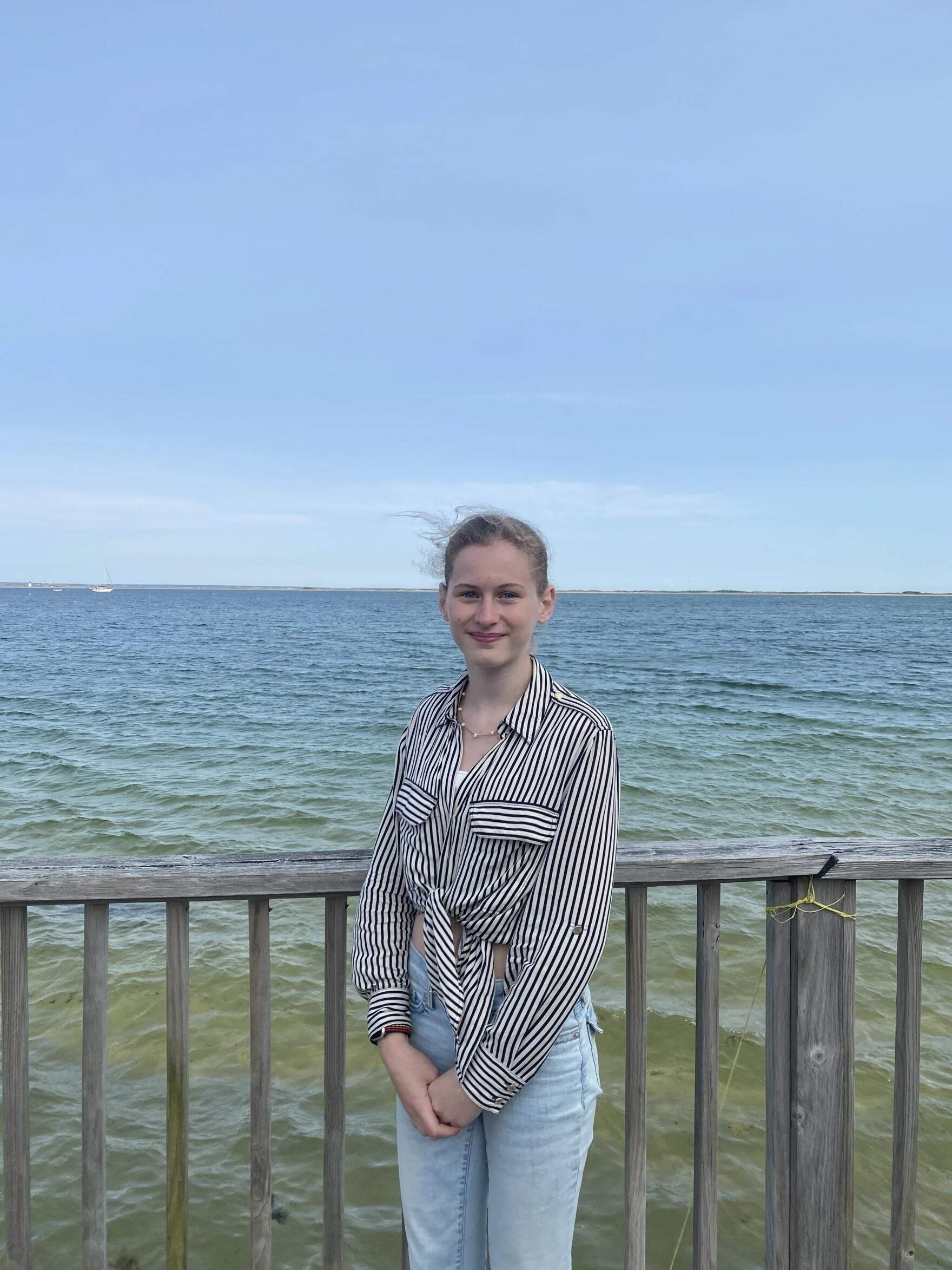 Provincetown IB Schools student Bella Wirthwein stands by the beach in front of her old house, which was floated across the inlet, June 2, 2025. (Samantha Watson/KYUK)