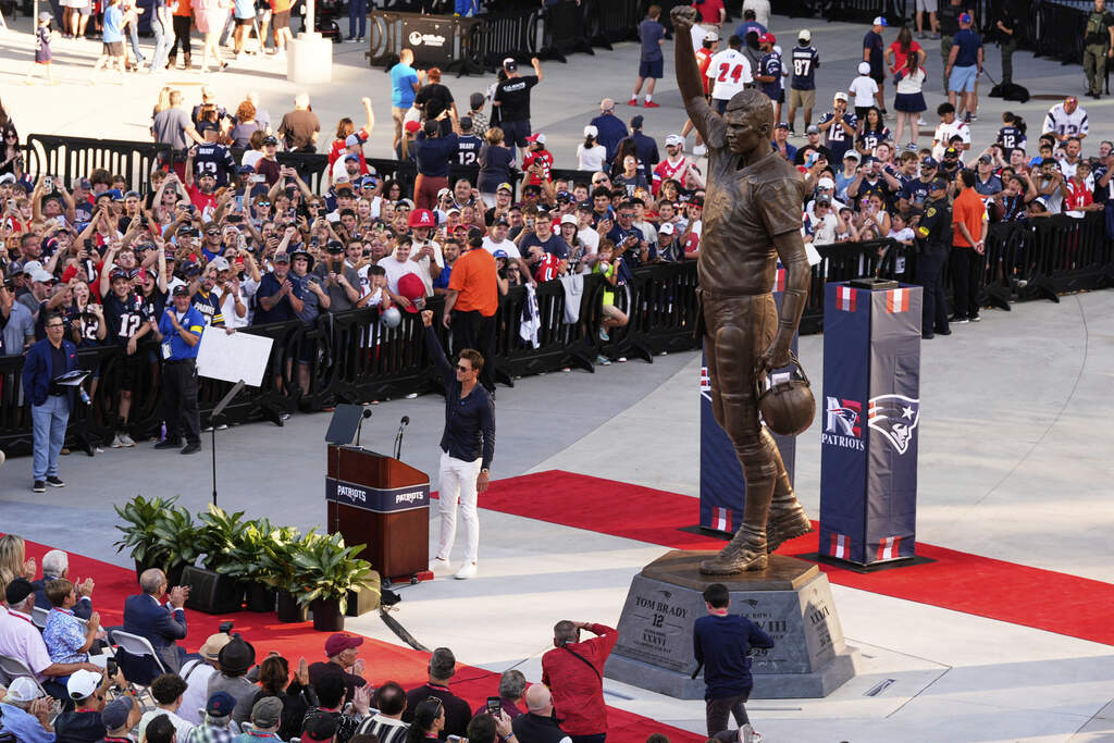 Tom Brady holds up a fist next to a new bronze statue of himself, Aug. 8, 2025, in Foxborough, Mass. (Charles Krupa/AP)