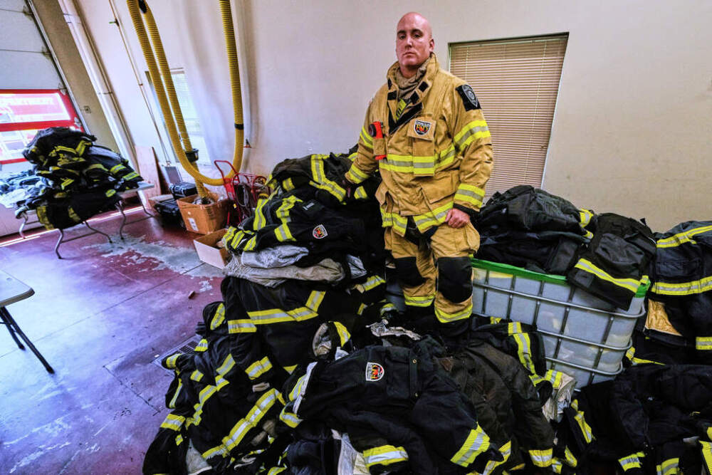Firefighter Christopher Harrington stands next to the station's old turnout gear, while wearing recently issued non-PFAS turnout gear, at Fire Station 4 in East Providence. (Charles Krupa/AP)