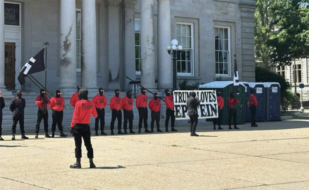 A photograph shared with NHPR shows the group carrying flags bearing swastikas and a sign that reads “Trump loves Epstein” outside of the New Hampshire State House on Aug. 2, 2025. (Courtesy of Victoria Farrell via NHPR)