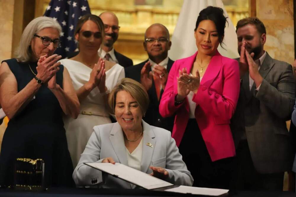 Gov. Maura Healey, flanked by advocates, lawmakers and others, signs the 2025 "shield" bill into law at the State House on Aug. 7, 2025. (Ella Adams/SHNS)