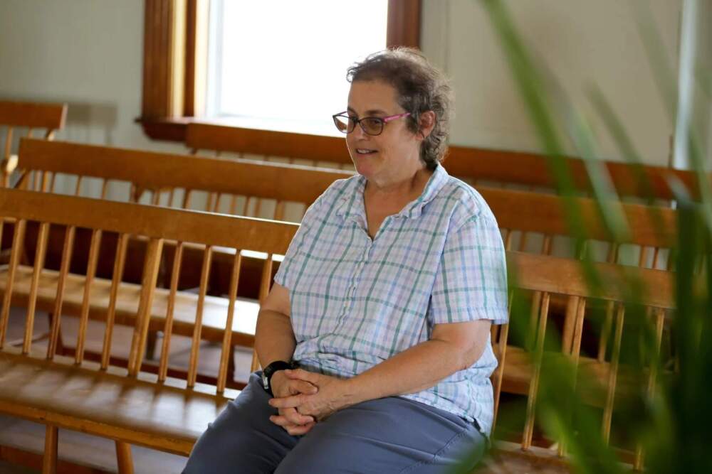Sister April Baxter, the newest Shaker, sitting on the benches in the Dwelling House Chapel where Sunday Meeting is held. (Esta Pratt-Kielley/Maine Public)