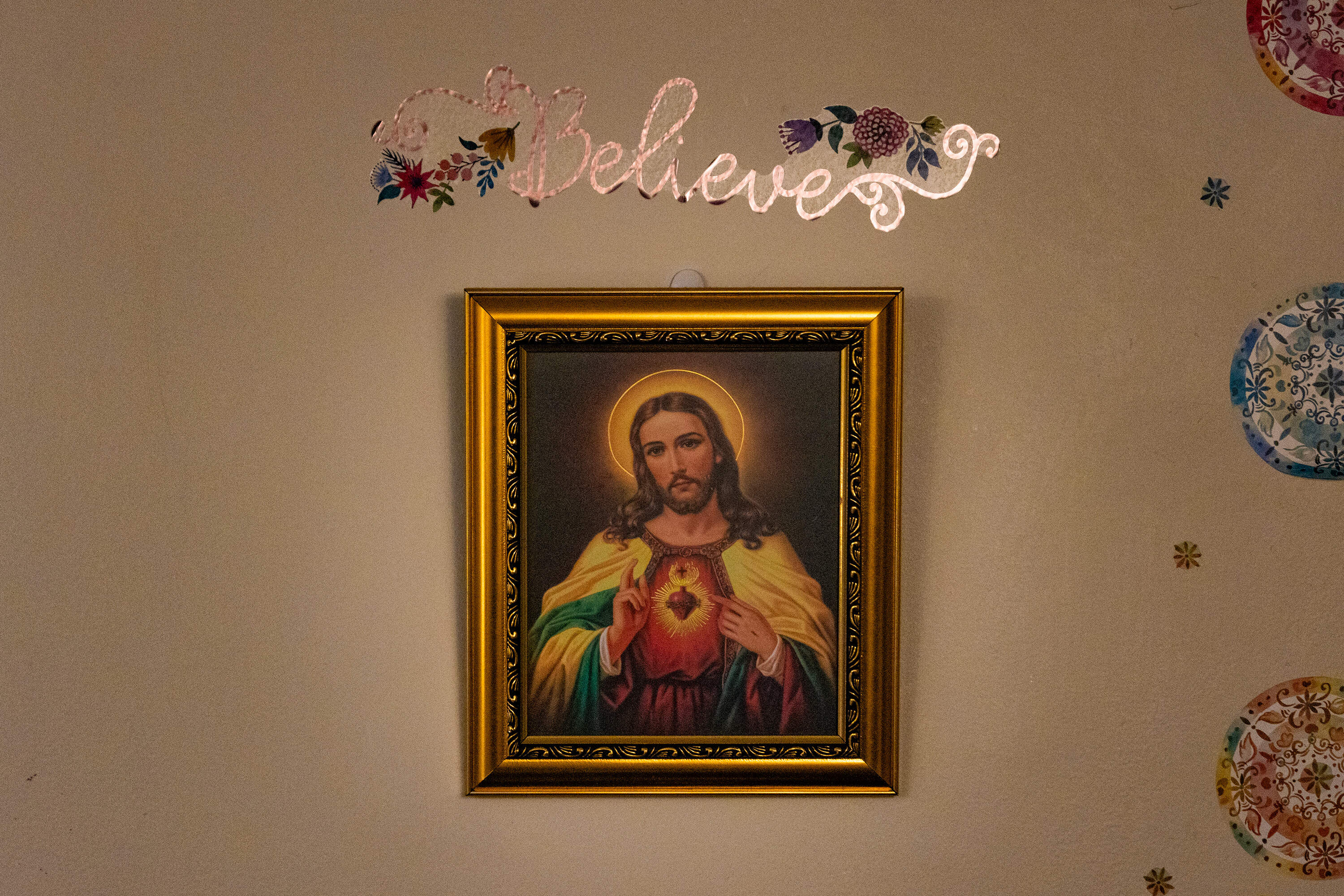 A foil decal of the word "Believe" hangs over a painting of Jesus in Louise's home. (Jesse Costa/WBUR)
