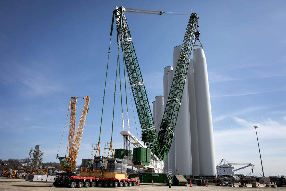 A crane moves wind turbine towers waiting to be moved out to sea at the Connecticut Port Authority's New London State Pier Terminal. (Robin Lubbock/WBUR)