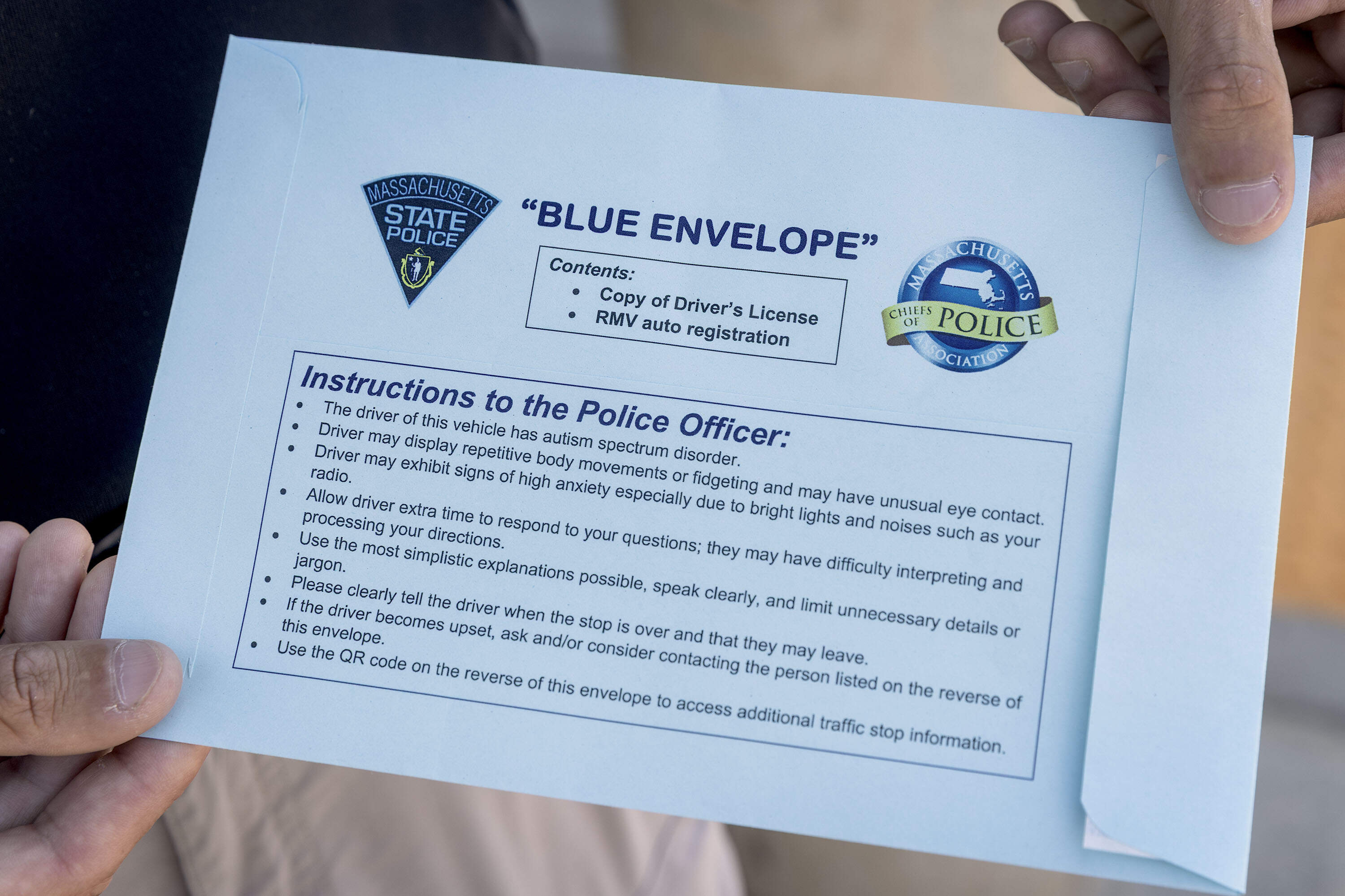 A State Police trooper holds a blue envelope with instructions that aim to assist officers during an incident involving a person with autism spectrum disorder. (Robin Lubbock/WBUR)