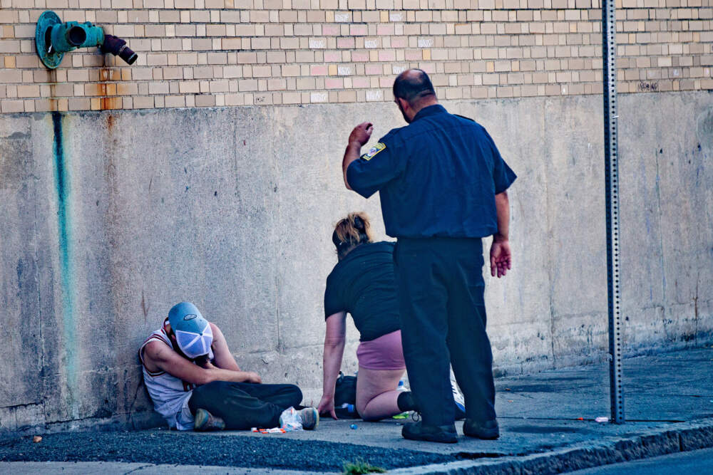 Newmarket Business Improvement District Public Safety Officer Mark Murphy helps a woman get up as he attempts to move her and another person away from a business on Atkinson Street. (Jesse Costa/WBUR)