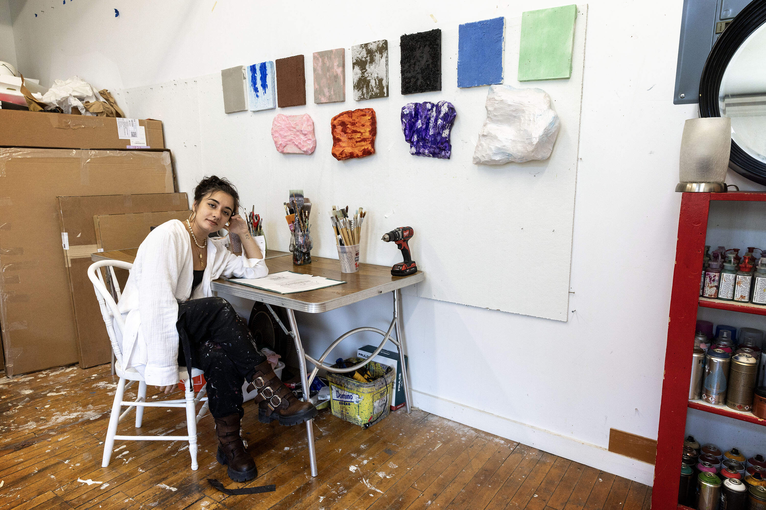 Nanajian at a desk in her studio next to a group of her wall-mounted sculptures. (Robin Lubbock/WBUR)