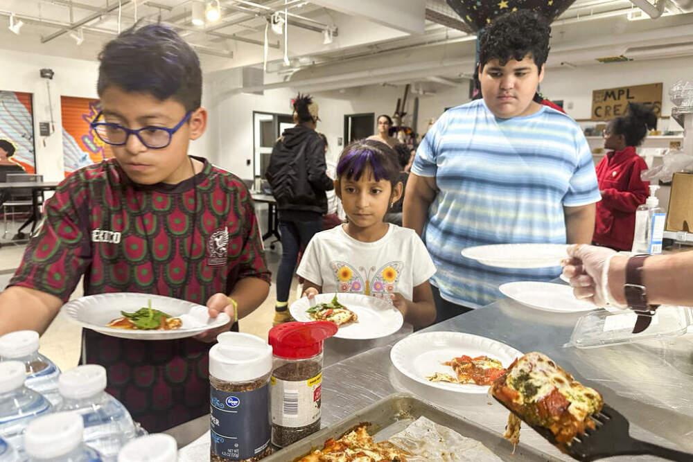 Attendees of an after-school nutrition program, Milwaukee Public Library Snack Hack, line up to get a slice of pizza made from scratch on Nov. 19, 2024. (Devi Shastri/AP)