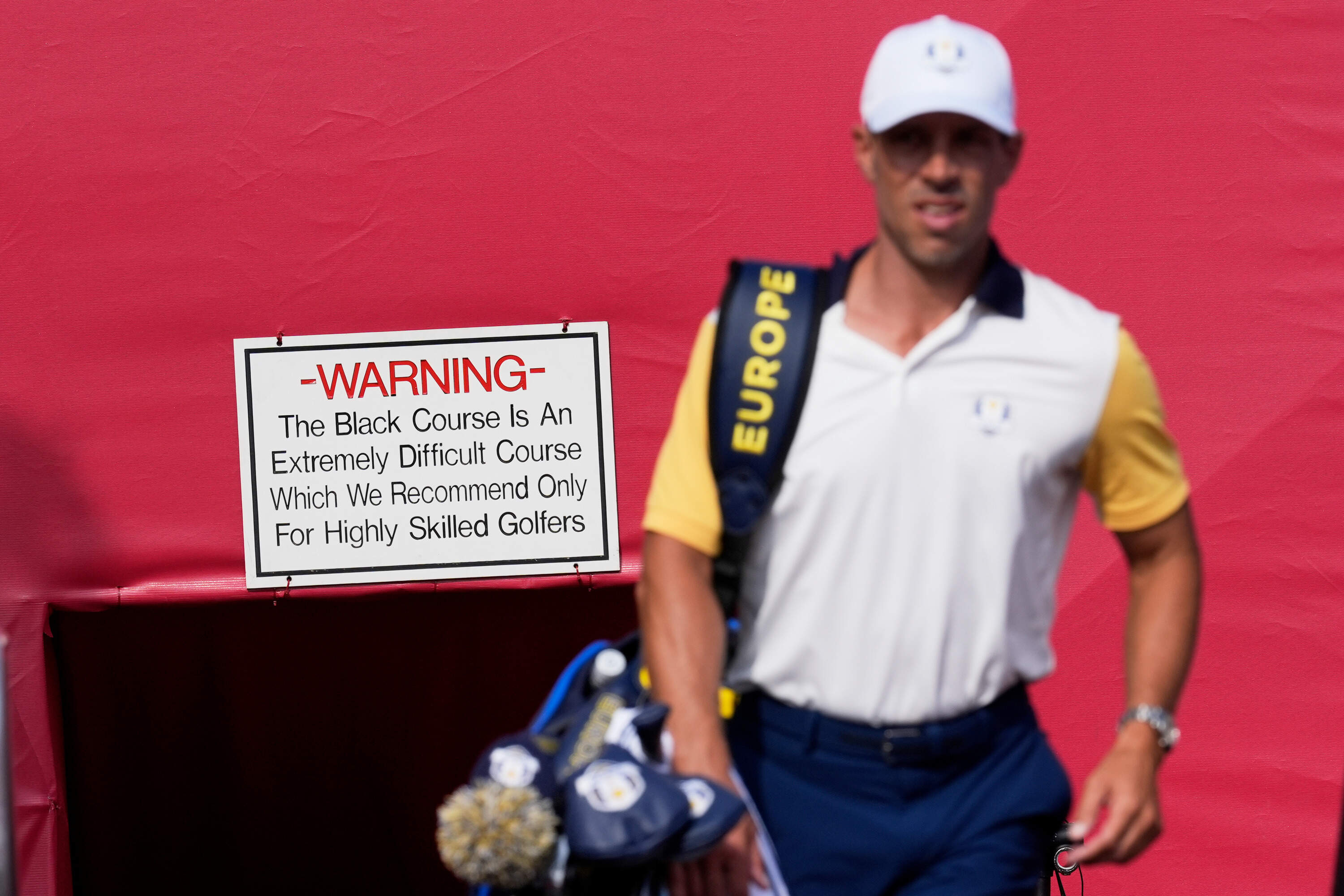 A caddie for Europe team walks near the sign warning golfers how difficult the courses is during a practice round for the Ryder Cup golf tournament, Tuesday, Sept. 23, 2025, in Farmingdale, N.Y., at Bethpage State Park's Black Course. (Robert Bukaty/AP)