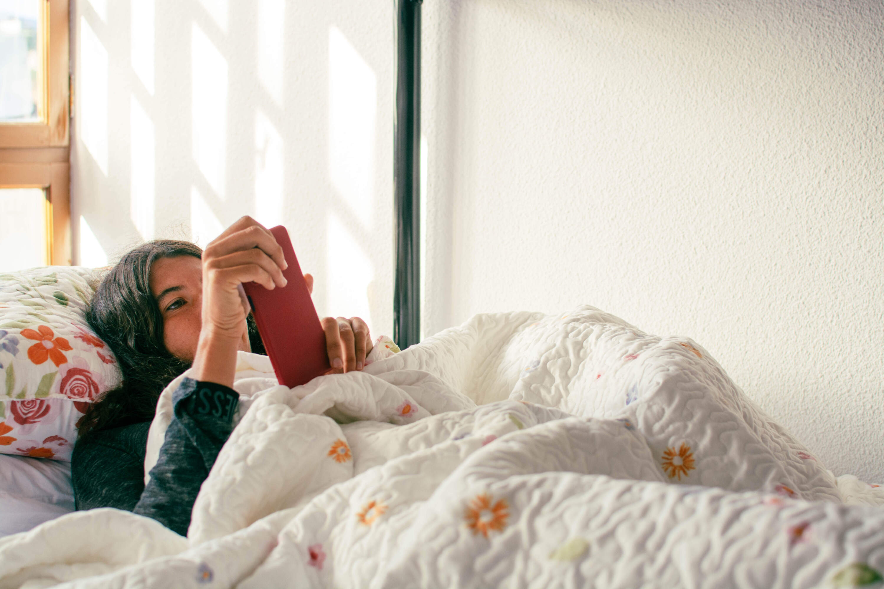 A woman lies in bed on her phone. (Crispin La Valiente/Getty Images)