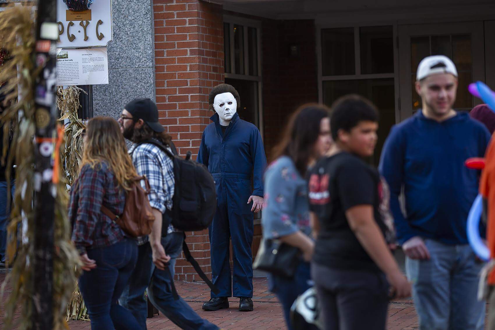 A steert performer portraying the role of Michael Myers from the horror classic “Halloween” stands amid visitors to Salem along Essex Street.