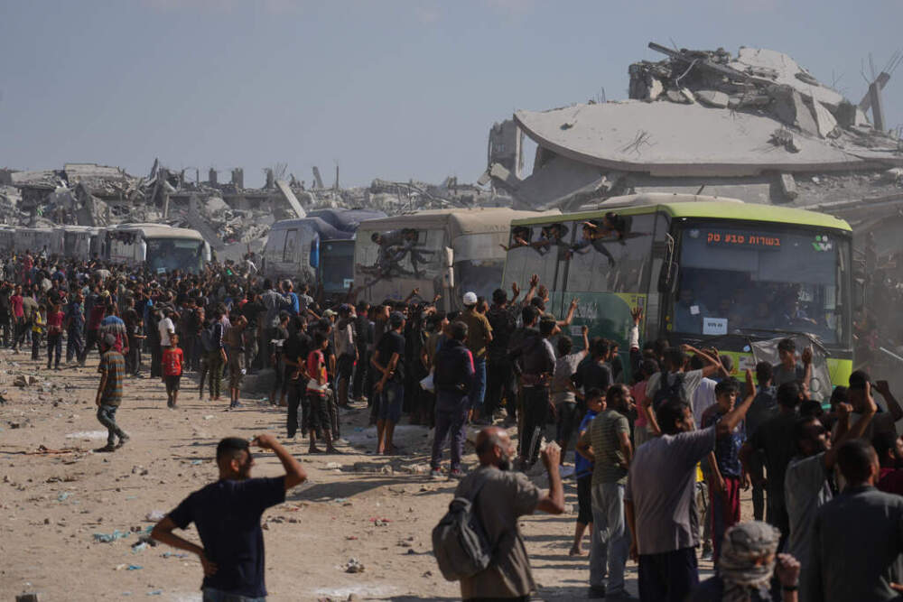 People greet freed Palestinian prisoners in buses past destroyed buildings in the Gaza Strip after their release from Israeli jails under a ceasefire agreement between Hamas and Israel, in Khan Younis, southern Gaza Strip, Monday, Oct. 13, 2025. (AP Photo/Jehad Alshrafi)