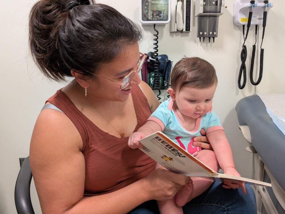 Karla Haney shows a book to her daughter, 9-month-old Elena Haney, before Elena receives flu and MMR vaccines at her pediatrician's office in Chelsea. (Priyanka Dayal McCluskey/WBUR)