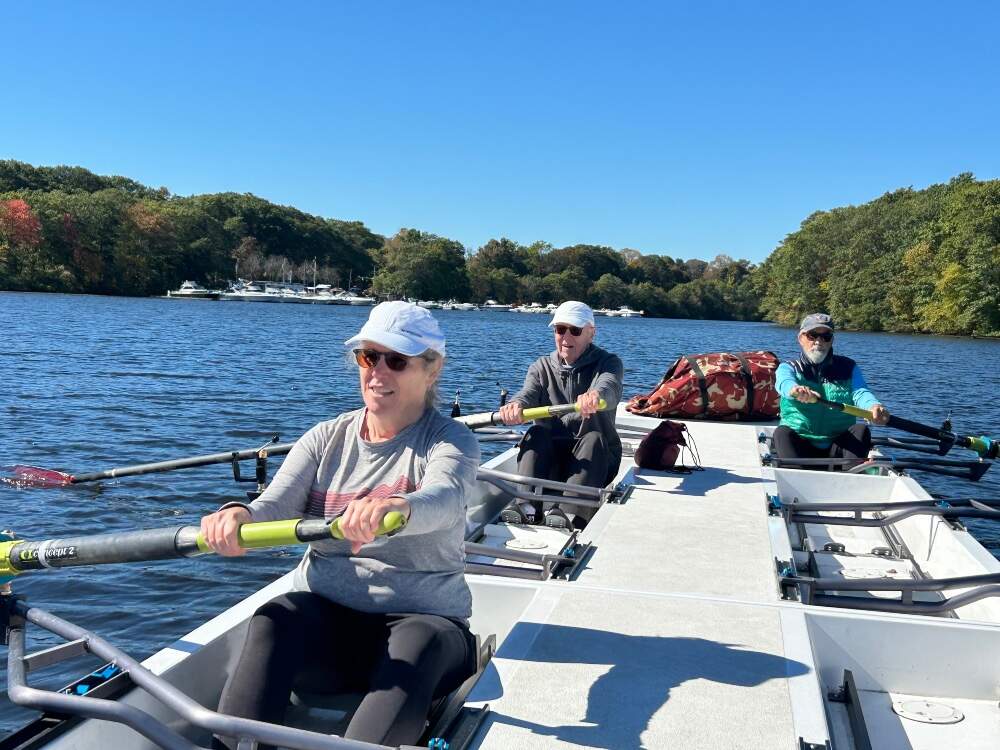 Caitrin Lynch (front left) and her father, Frank Lynch (back left) training for the octogenarian eight-boat that will row a racing shell to the team competing in the Head of the Charles, alongside Andy Anderson (right), who will compete on the racing boat. Boston, 2025. (Photo by Catherine Saarela, courtesy Caitrin Lynch)