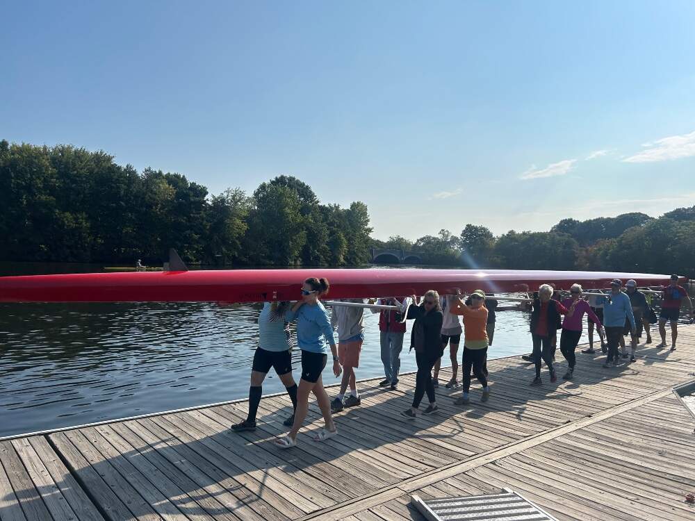 A group of rowers at CRI, including Frank and Caitrin Lynch, carrying the eight-boat shell. Boston, 2025. (Photo by Catherine Saarela, courtesy Caitrin Lynch)