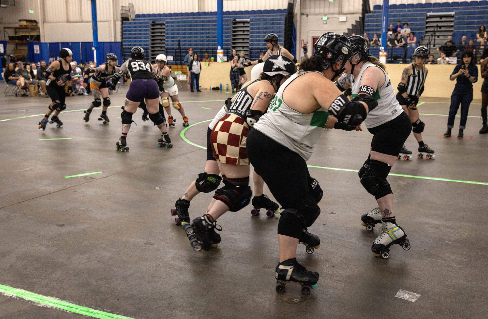 Jammers, wearing helmets with a star, attempt to push through groups of opposing blockers at a roller derby game in Wilmington, Mass. (Robin Lubbock/WBUR)