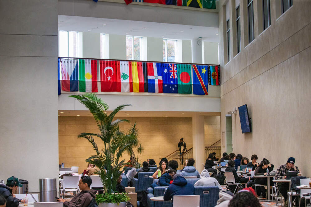 Students lounge in the Campus Center at UMass Boston beneath rows of the flags of international countries. (Jesse Costa/WBUR)