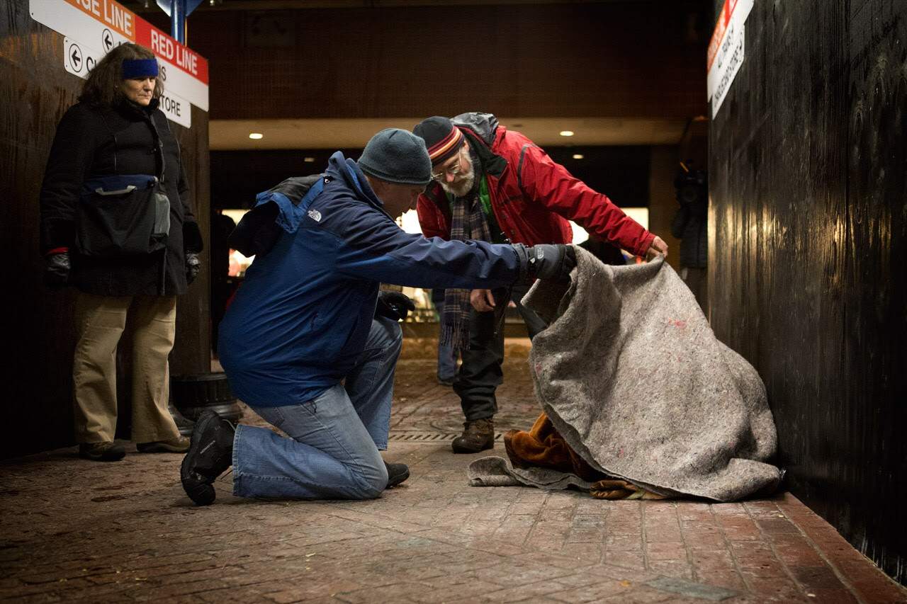 Jim Greene, the director of emergency shelters for the Boston Public Health Commission (in red), and a volunteer lift a blanket off of a homeless woman at Downtown Crossing to check if she is OK. (Jesse Costa/WBUR)