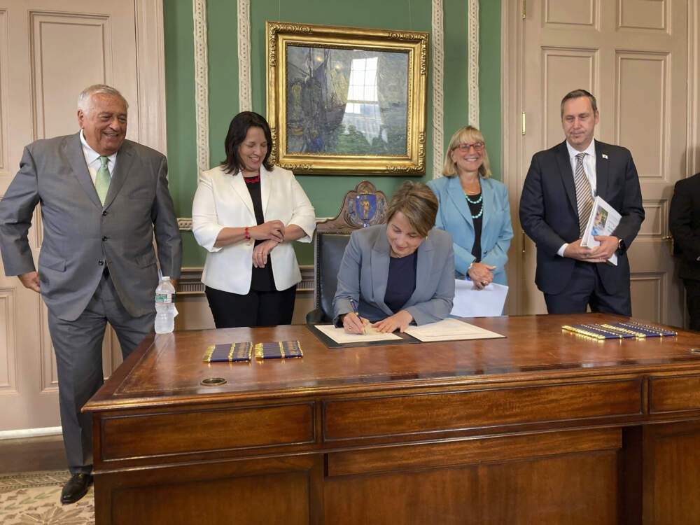 Massachusetts Gov. Maura Healey signs the overdue state budget for the 2024 fiscal year on Aug. 9, 2023. Looking on are, from left, House Speaker Ronald Mariano, Lt. Gov. Kim Driscoll, Senate President Karen Spilka – all Democrats along with Healey, and Administration and Finance Secretary Matthew Gorzkowicz. (Steve LeBlanc/AP File)