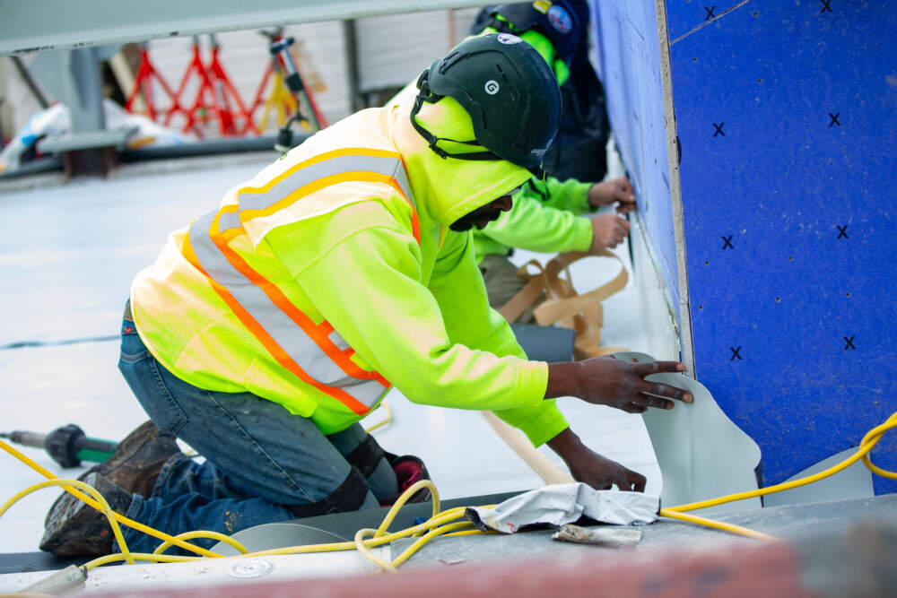 Workers install a white reflective single-ply membrane on the roof for better energy efficiency. (Jesse Costa/WBUR)