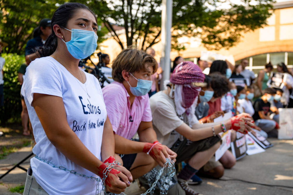 Ambar Santiago-Rojas of Connecticut Students for a Dream kneels in New Haven, Conn. in July 2025 at the head of a line of students who wear chains and have blood painted on their hands. They and other protesters gathered to demand the return of Esdrás, a rising Junior at Wilbur Cross High School in New Haven. Esdrás was detained by ICE while at work the week before. (Tyler Russell/Connecticut Public)