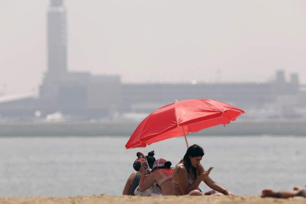 Smoke from Canadian wildfires obscures the control tower at Logan International Airport behind people sitting on Constitution Beach in Boston on July 1, 2023. (Michael Dwyer/AP)