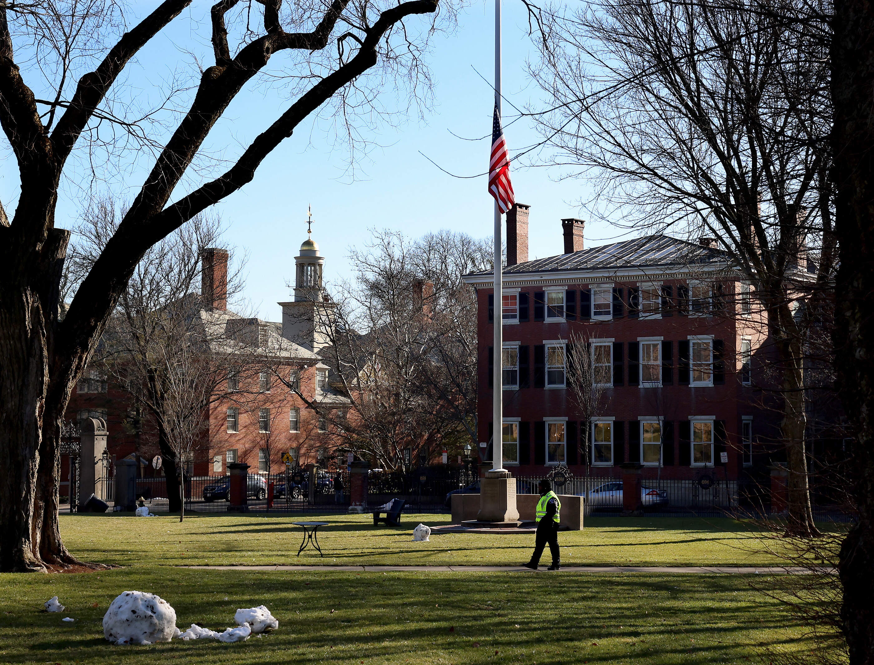 A security guard walks past a flag at half-staff on the main green of Brown University in Providence on Dec. 18. (Mark Stockwell/AP)