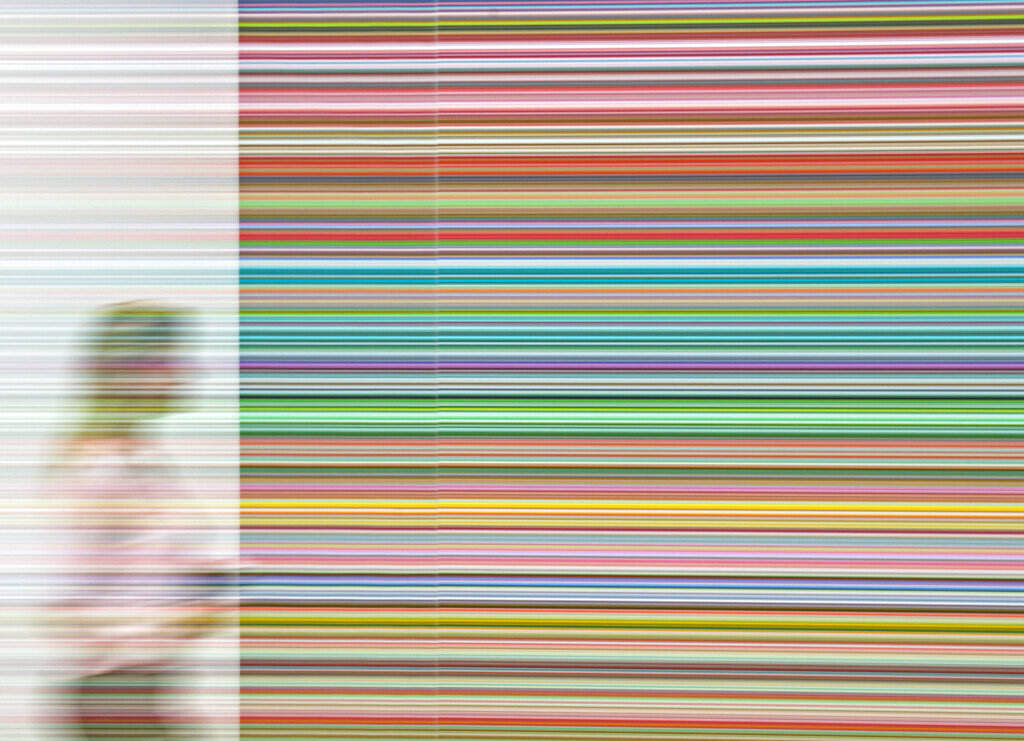 In this picture taken with a long-time exposure a woman is reflected in the glass of an installation in front of the work 'Strip' (927-9), (2012) by Gerhard Richter during a press preview in his exhibition 'Gerhard Richter' by the Gallerie Neue Meister (New Master Gallery) at the Albertinum in Dresden, eastern Germany, Wednesday, Feb. 25, 2015. (AP Photo/Jens Meyer)