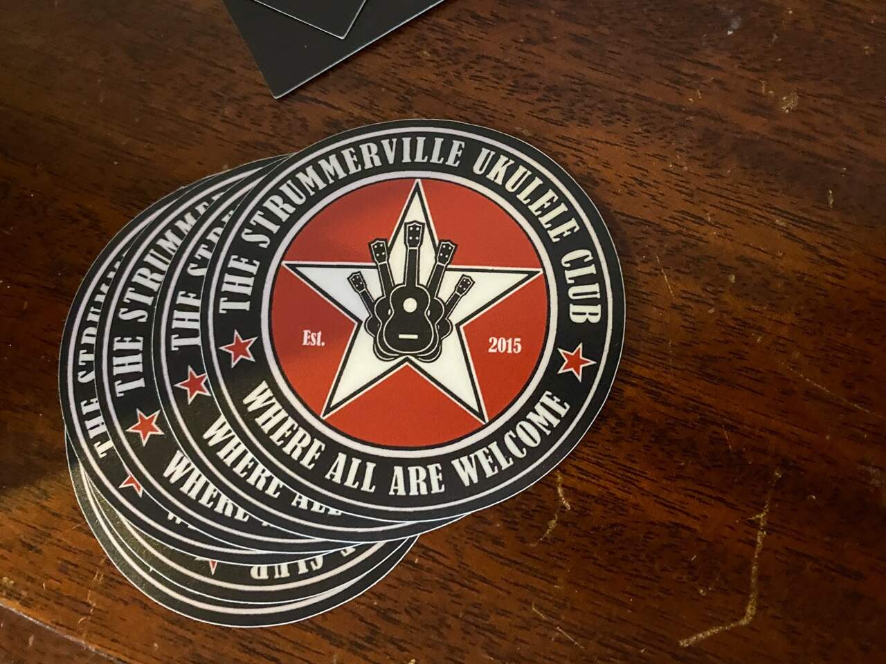 Stickers up for grabs at a meetup of the Strummerville Ukulele Club. "Where all are welcome," they read — one of the group's mottos. (Sharon Brody/WBUR)