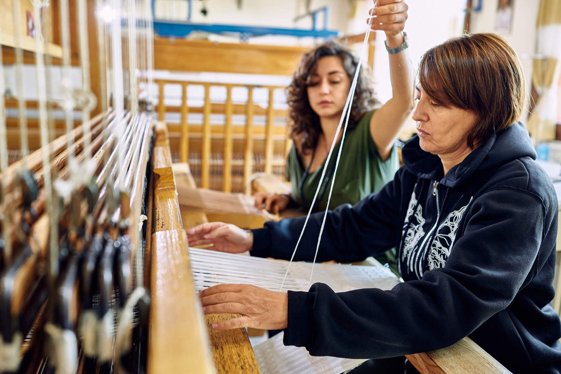 Two women weave fabrics on a handloom at San Patrignano. (Wilson Santinelli for WBUR)