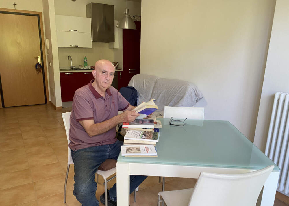 Paolo Severi sits at his kitchen table with books about scandals at San Patrignano scattered in front of him. (Deborah Becker/WBUR)