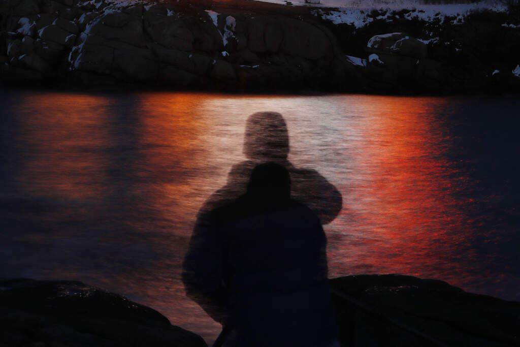 In this photo made with a long exposure, a man is silhouetted against lights reflected in the waters off Cape Neddick in Maine on Dec. 11, 2017. (AP Photo/Robert F. Bukaty, File)