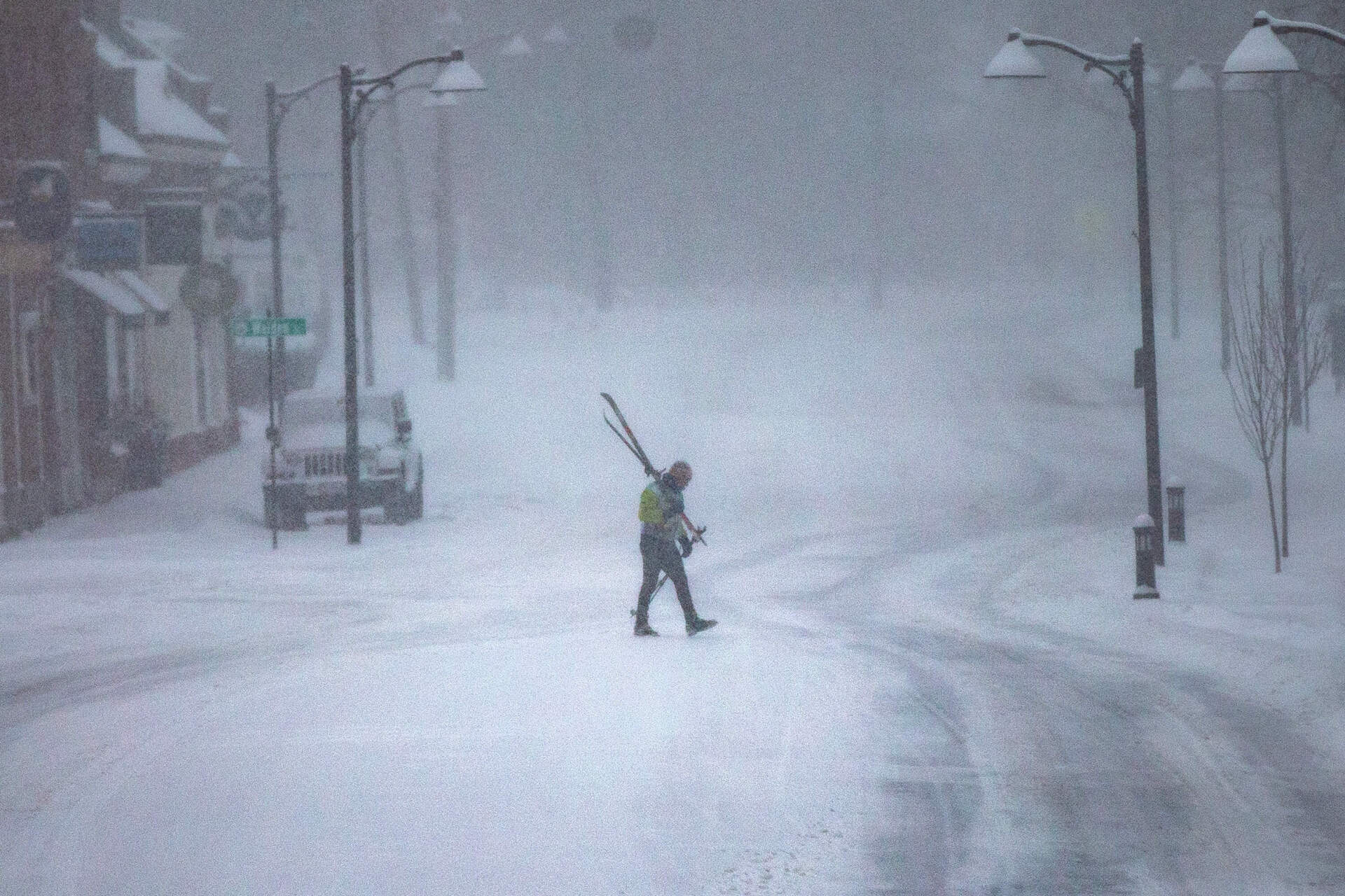 A man with cross country skis walks across Main Street in Concord on Sunday, Jan. 25, 2026. (Jesse Costa/WBUR)