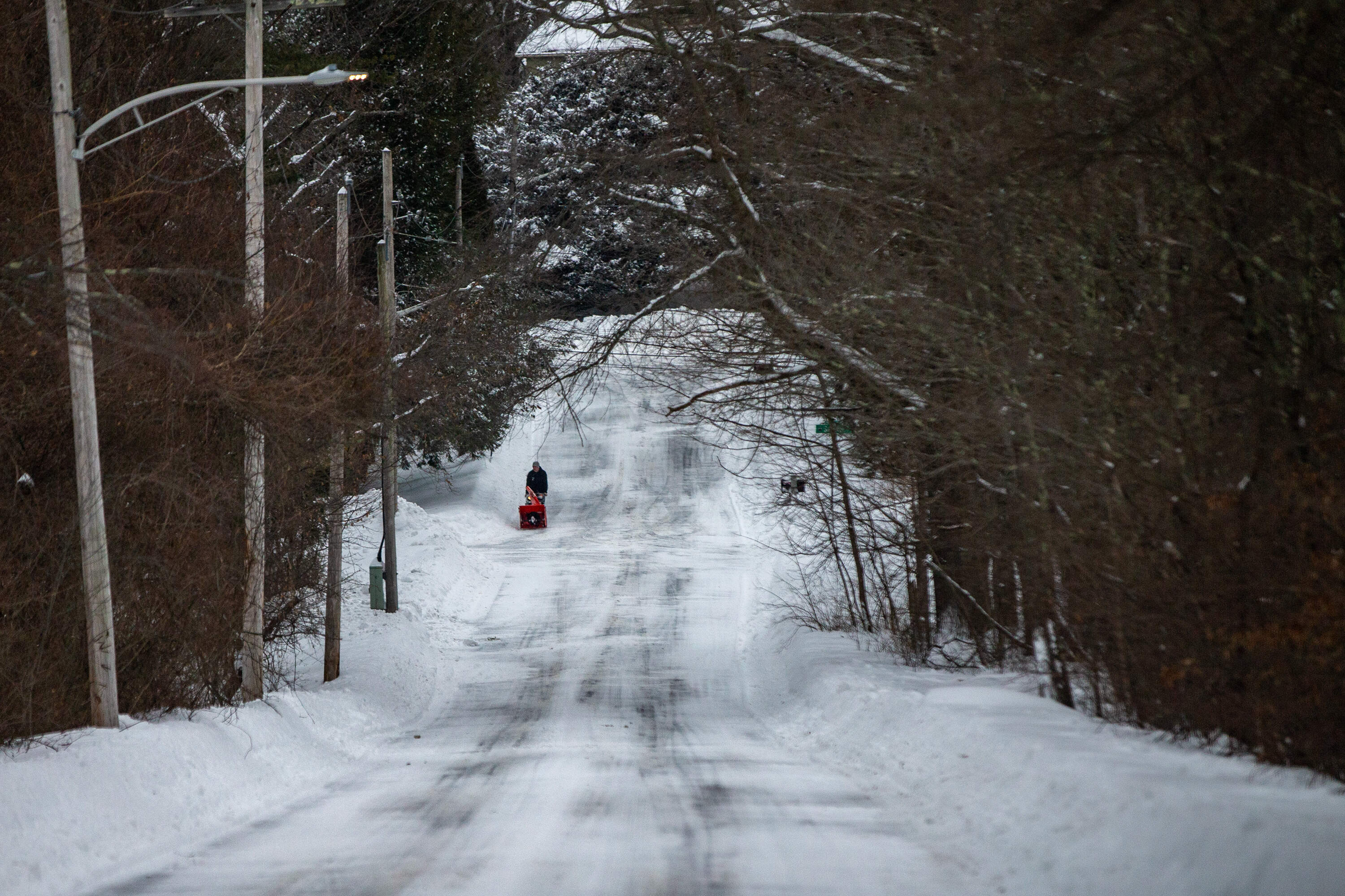 A man pushes a snow blower as he walks down Nawshawtuc Road in Concord the following morning after the first major snowstorm of the year. (Jesse Costa/WBUR)