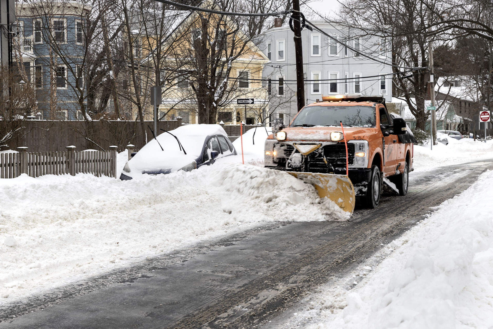 A snowplow clears Cambridge streets alongside snow-covered cars. (Robin Lubbock/WBUR)