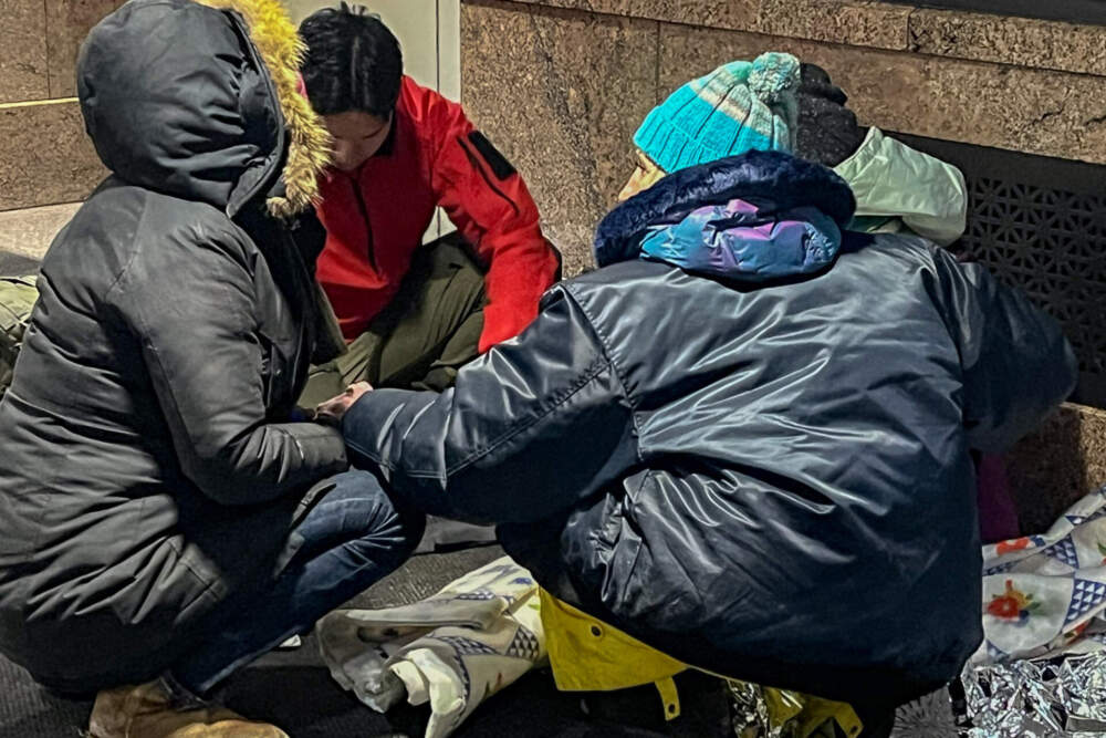 Suzanne Fareri-Early and Bowen Popkin, a COPE volunteer who is also an EMT, assist a woman whose fingers are bordering on frostbite (right) and talk with the woman's concerned friend. (Lynn Jolicoeur/WBUR)